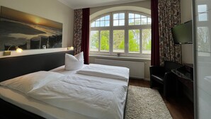 Ein Hotelzimmer mit einem großen Bett, einem Schreibtisch, einem Fernseher und einem Fenster mit Vorhängen.