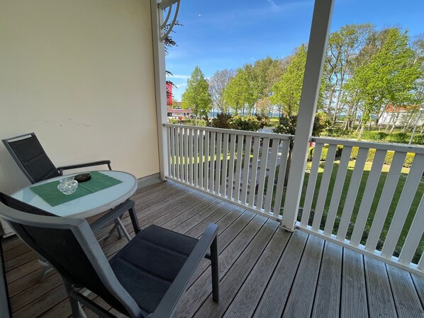 A covered outdoor area with a table and chairs, a white railing, and a view of trees and buildings.