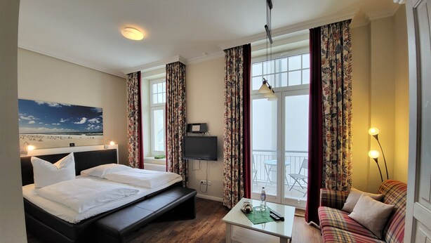 A hotel room with a bed, a TV, a balcony with chairs, and a sofa.