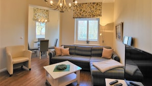 Ein Wohnzimmer mit einer Couch, einem Sessel und einem Couchtisch. Es gibt eine Kandelaber, ein Fenster mit Aussicht und eine Lampe.