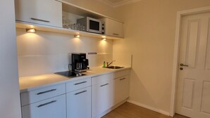 A compact kitchen with white cabinets, a built-in microwave, a coffee maker, and a sink.