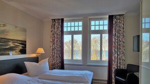 A hotel room with a large bed, a desk, a chair, and a view of trees through the window.