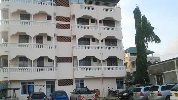 A multi-story building with balconies, parked cars, and a motorcycle.