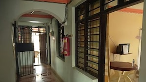 A hallway with a tiled floor, a fire extinguisher mounted on the wall, and a small table with a chair.