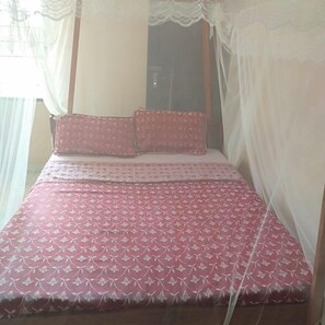 A bed with a floral patterned bedspread and two pillows, a canopy, and sheer curtains. - Miritini guest house & restaurant (Mombasa)