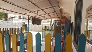 A covered outdoor seating area with a metal roof, a Coca-Cola refrigerator, and a fence with colorful vertical slats.