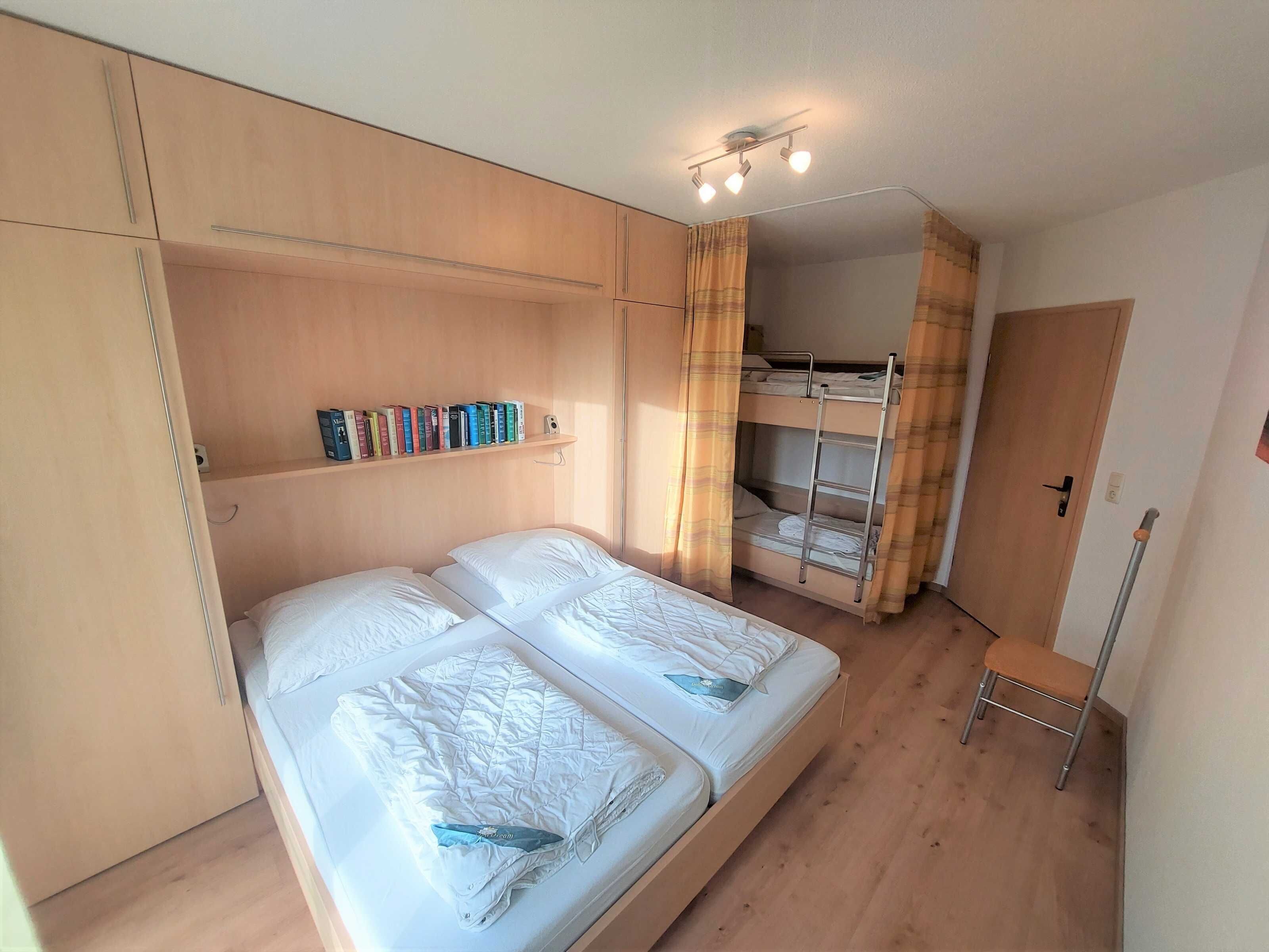 Una camera da letto con un letto grande, un letto a castello, scaffali di legno con libri e una piccola sedia.