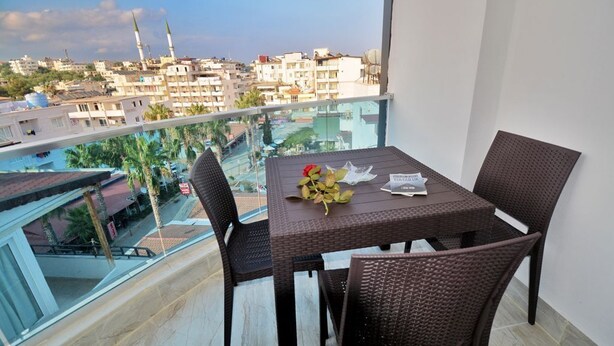 A balcony with a table and chairs, overlooking a cityscape with buildings and a mosque. - Palmiye Otel 2 (Erdemli)