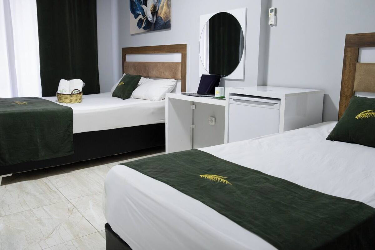 A hotel room with two beds, a desk, a mirror, and a painting on the wall.