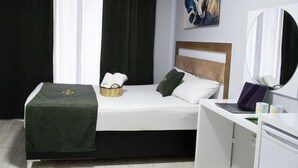 A hotel room with a bed, a desk with a laptop, a basket with towels, and a painting on the wall. - Palmiye Otel 2 (Erdemli)