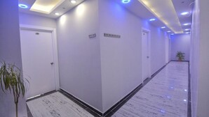 A hallway with white walls, black-tiled flooring, and recessed lighting. There are doors on the left and right, and a potted plant in the center. - Palmiye Otel 2 (Erdemli)