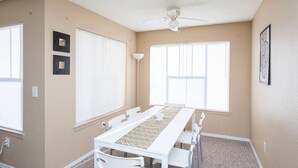 A room with a long table, two windows with blinds, a ceiling fan, and a framed picture on the wall. - Charmant Cosy et Design Vaucresson Séjour (Vaucresson)