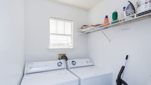 A laundry room with two front-loading washers, a window, a shelf with cleaning supplies, and a vacuum cleaner. - Charmant Cosy et Design Vaucresson Séjour (Vaucresson)