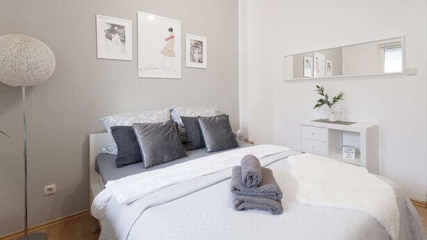 A bedroom with a bed, pillows, a bedside table, a mirror, and wall art. - Charmant Cosy et Design Vaucresson Séjour (Vaucresson)