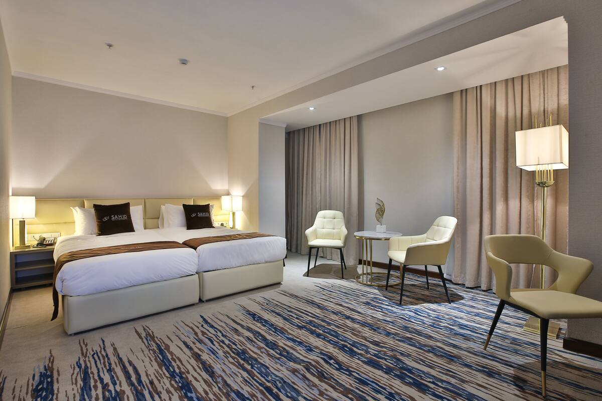 A hotel room with a large bed, two bedside tables, a desk with a chair, a small round table, and a lamp.