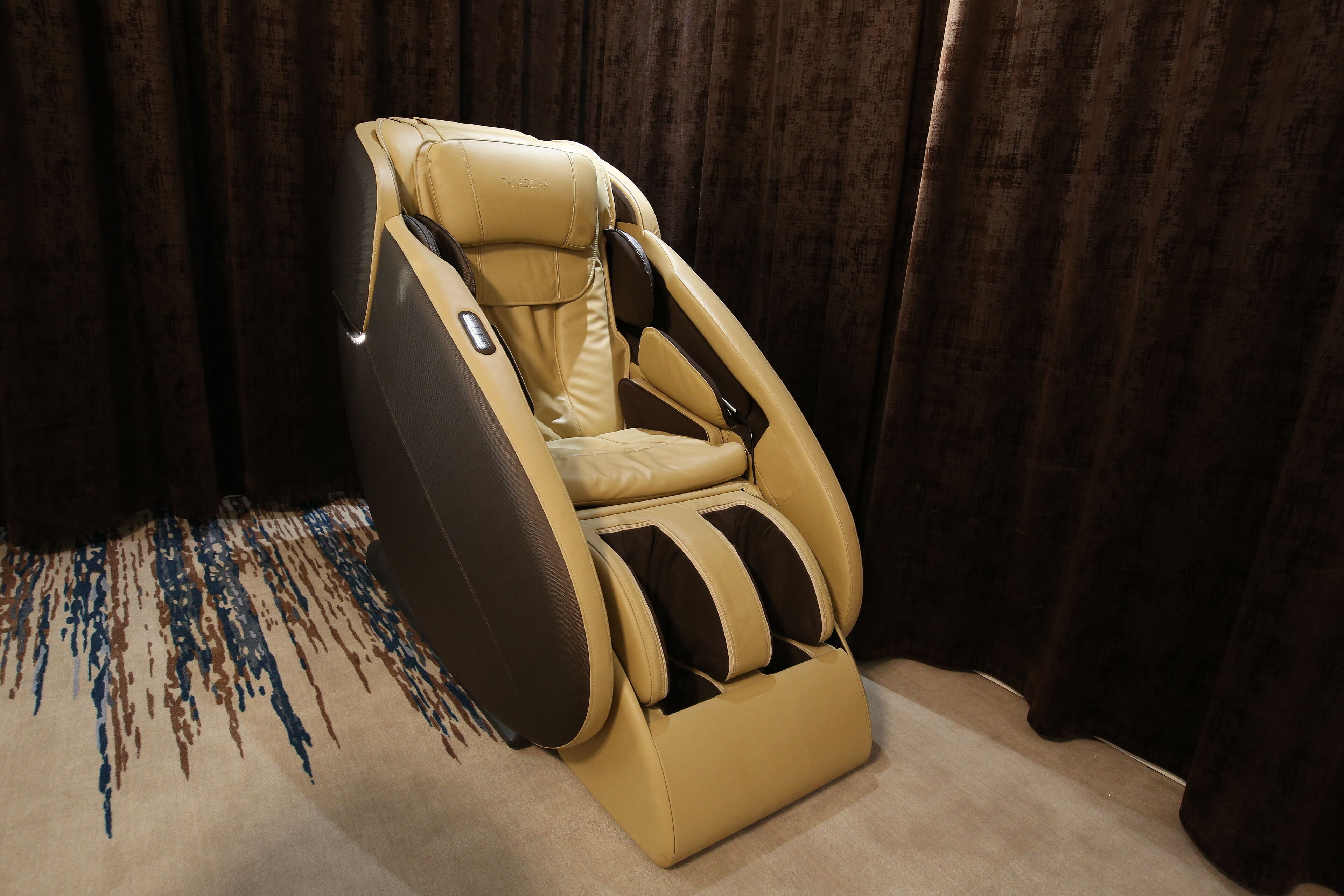 A massage chair with a reclining backrest and footrest, positioned in a room with dark curtains.