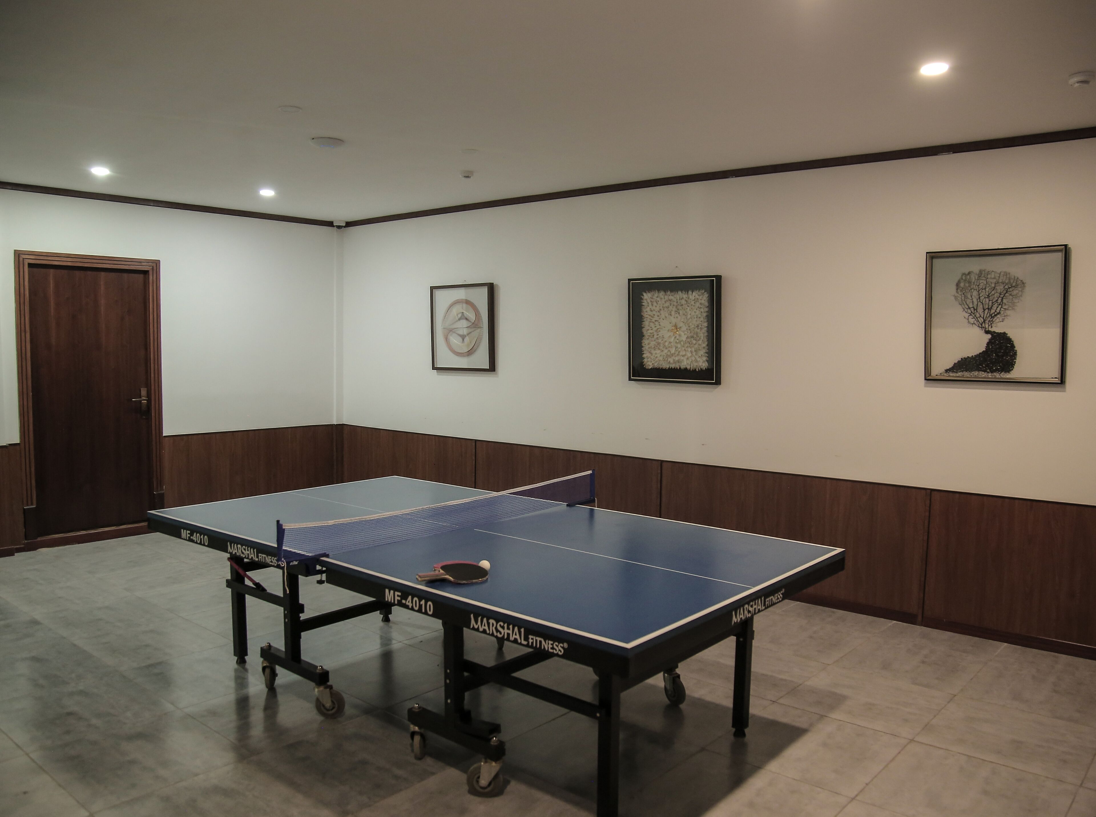 Una mesa de ping pong con ruedas, una puerta y obras de arte enmarcadas en las paredes.