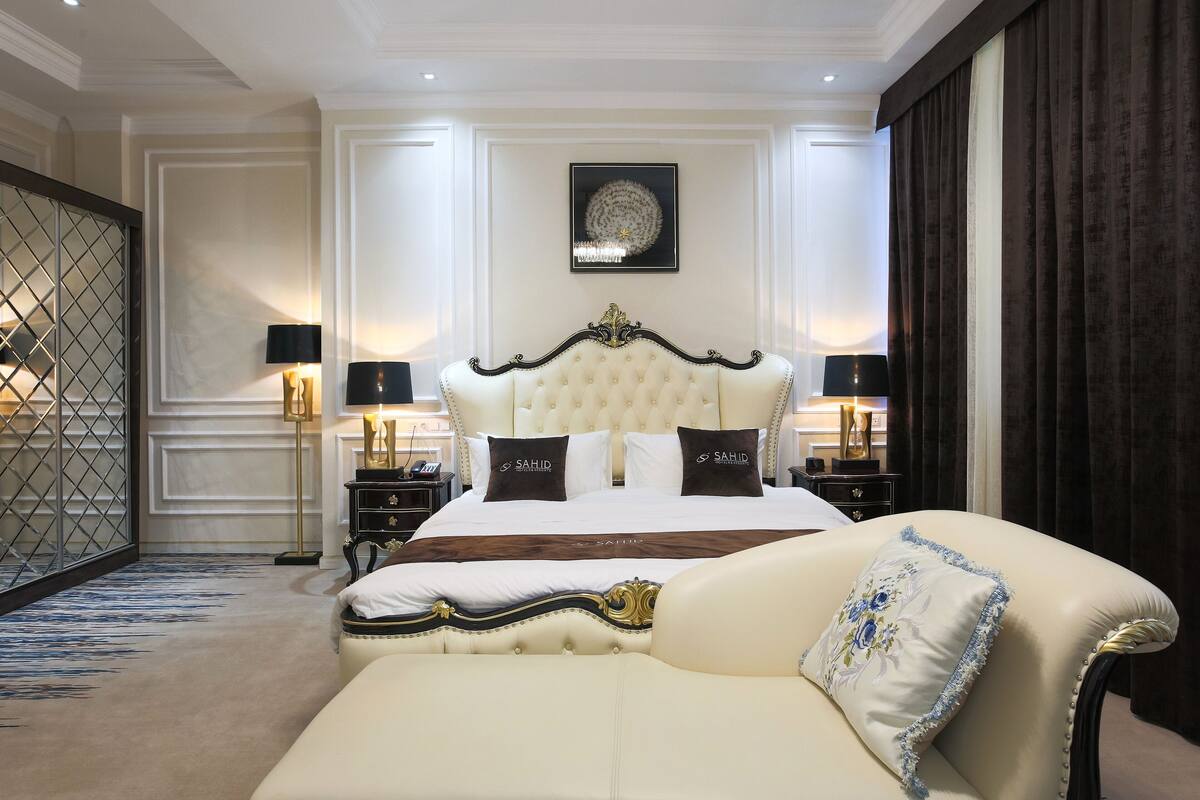A luxurious bedroom with a large bed, ornate headboard, and a plush sofa.