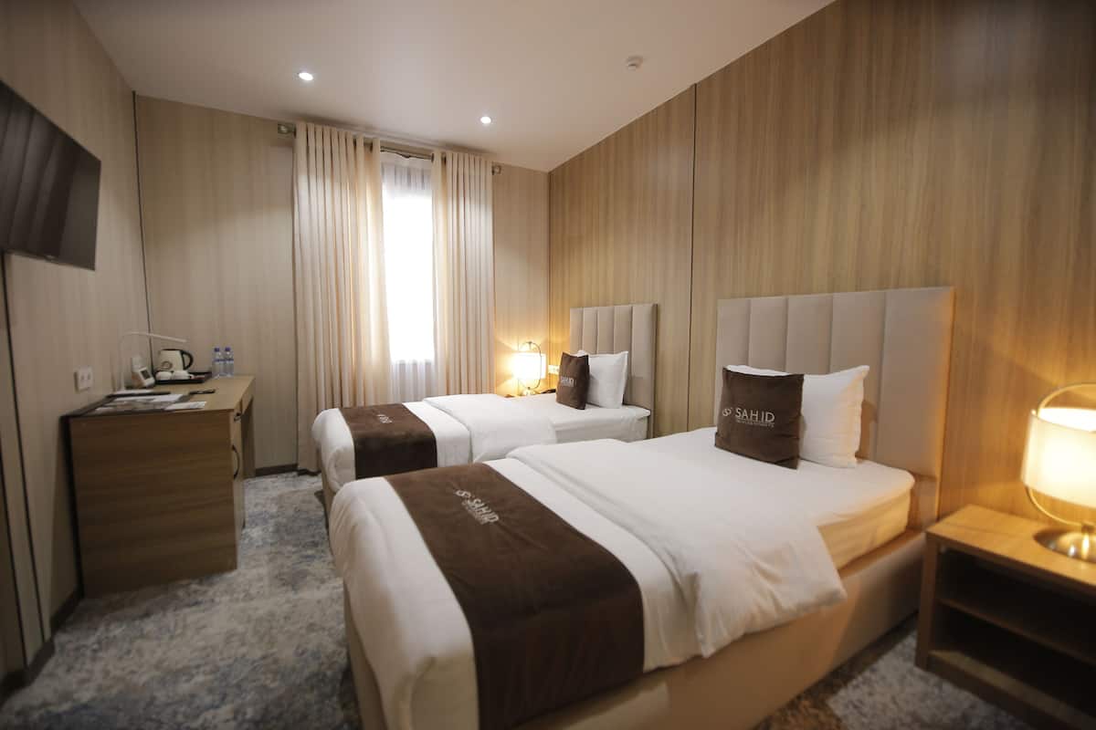 A hotel room with two beds, a desk, a TV, and a lamp.