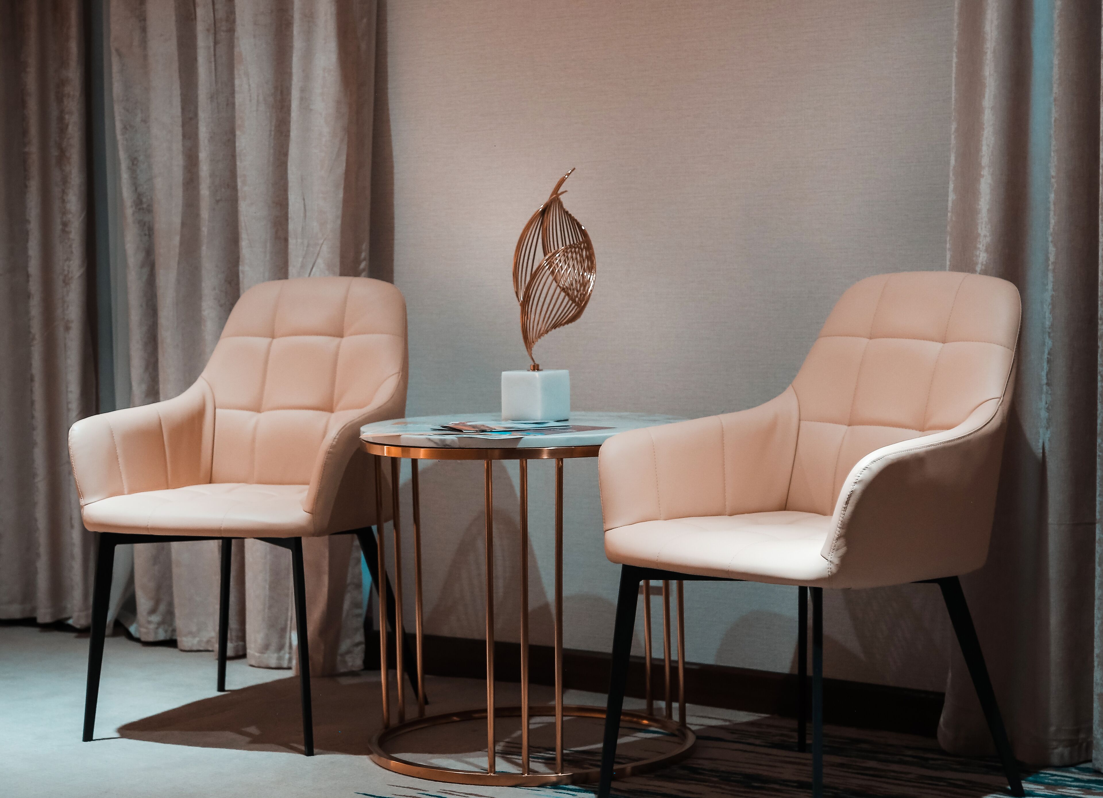 Two cushioned chairs with a small table between them, a decorative plant, and a curtain in the background.