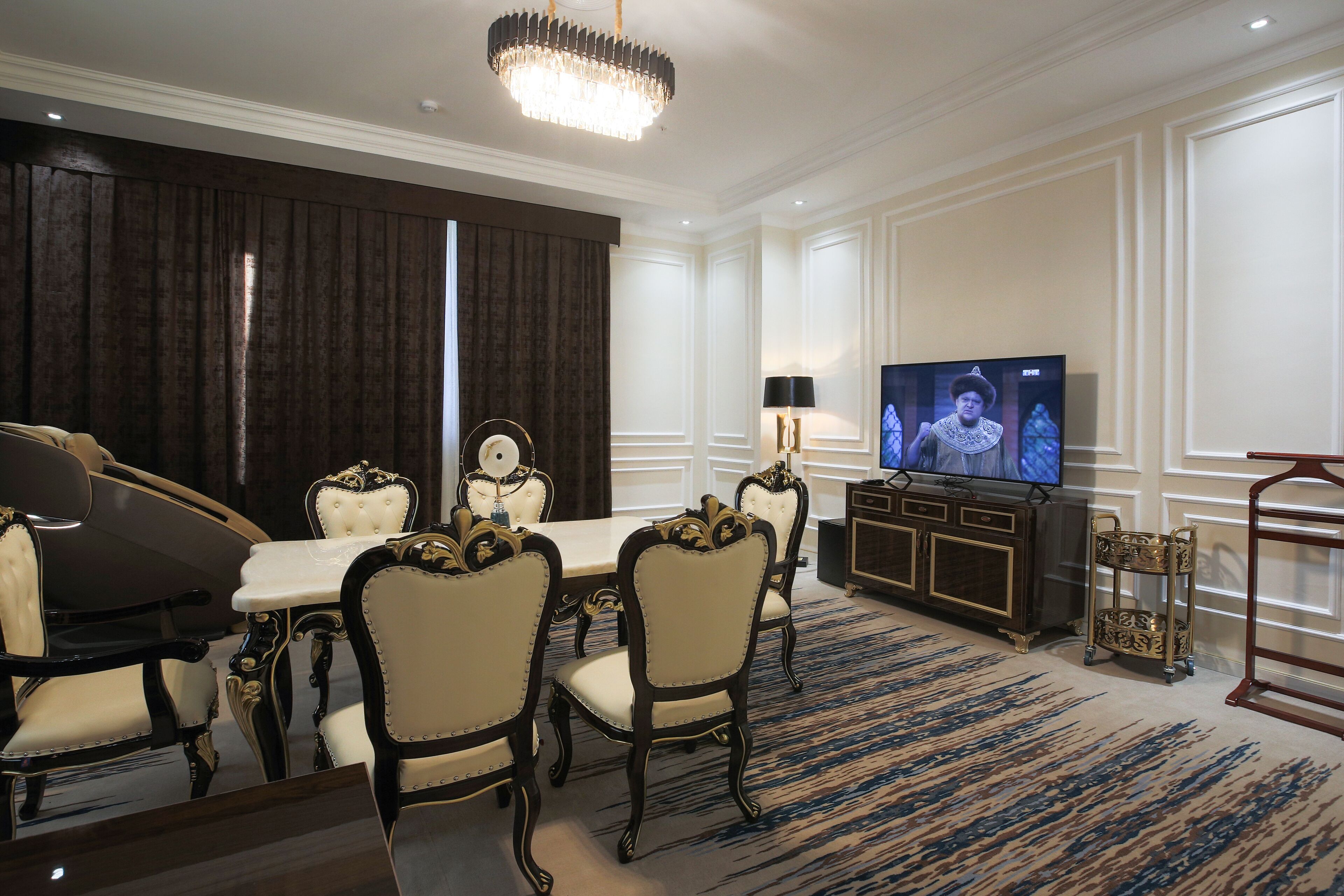 A formal dining room with a large table, ornate chairs, a television, and a chandelier.