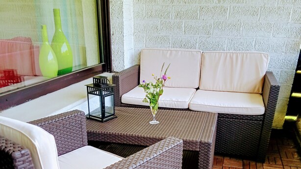 A wicker sofa set with cushions, a small table with a vase of flowers, and a tiled floor. - Family & dog-friendly vacation apartment Hahnenklee with balcony near hiking trails (Goslar)