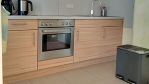 A modern kitchen with wooden cabinets, a stainless steel oven, a coffee maker, and a trash bin. - Family & dog-friendly vacation apartment Hahnenklee with balcony near hiking trails (Goslar)
