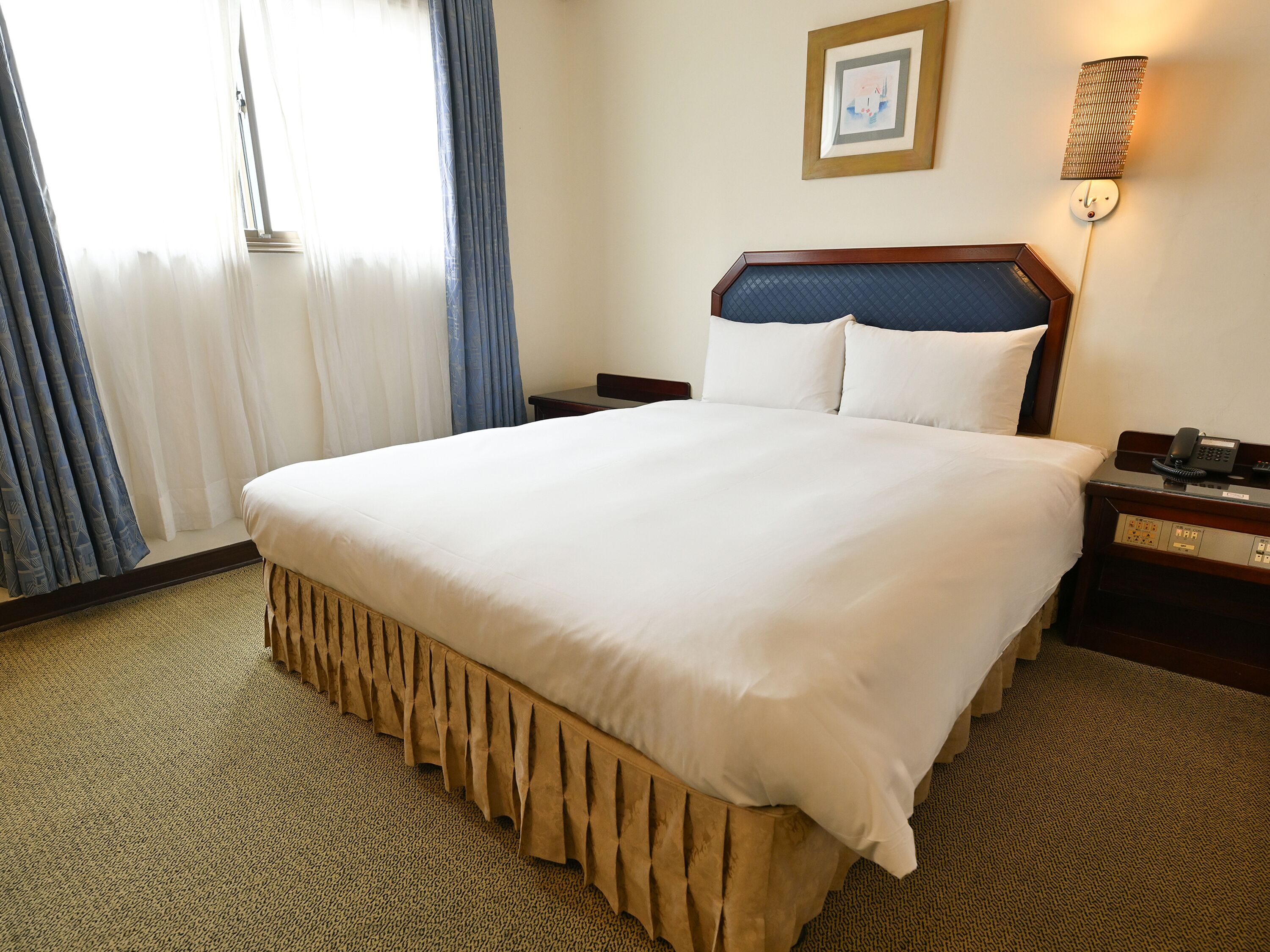 A hotel room with a large bed, a bedside table, a lamp, and a framed picture on the wall.