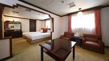 Habitación de hotel con cama, escritorio, silla, mesa de centro y un gran ventanal con cortinas.