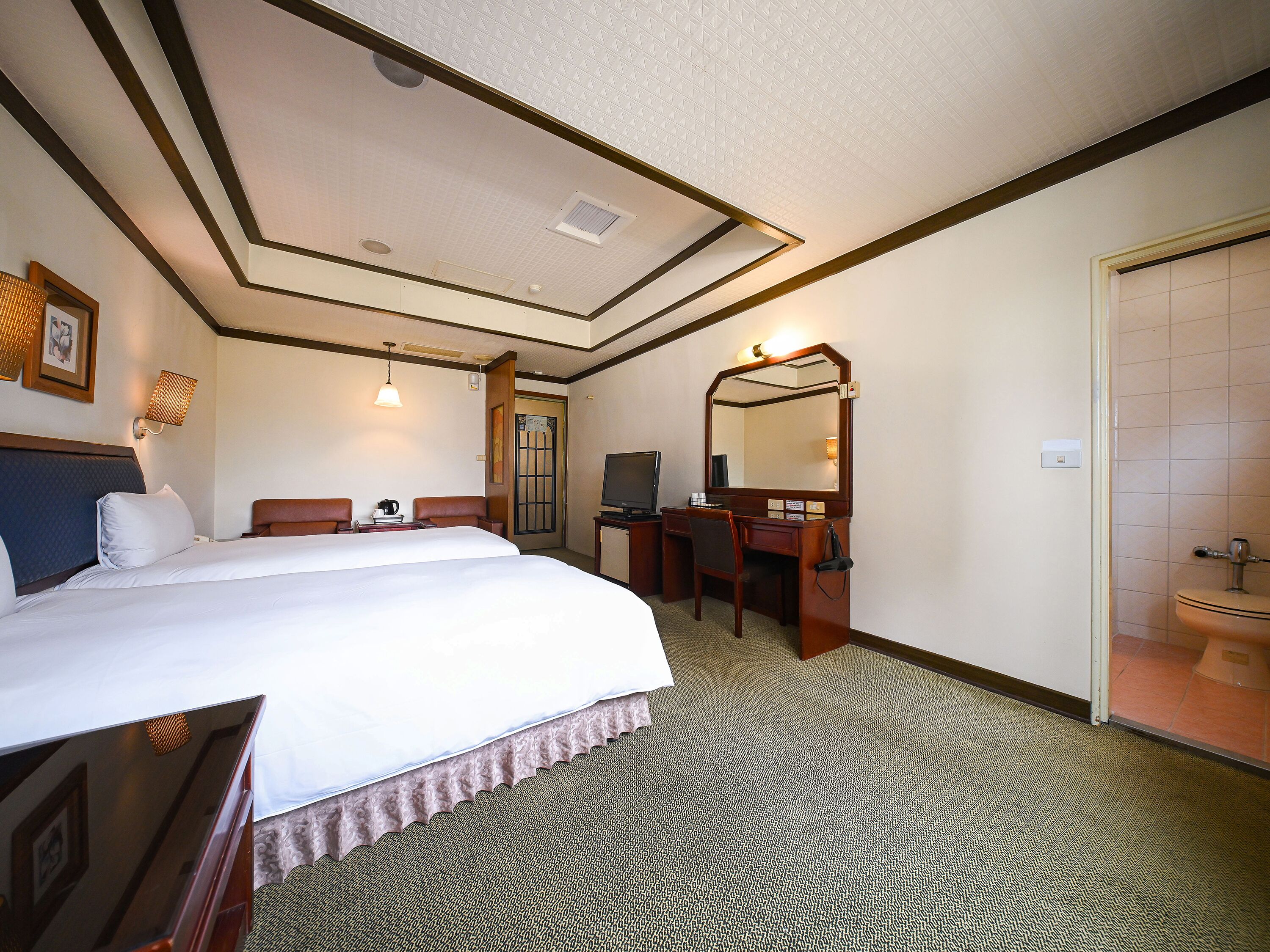 A hotel room with a large bed, a desk with a chair, a television, a mirror, and a bathroom.