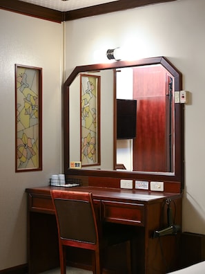 Habitación de hotel con un escritorio de madera, una silla, un espejo grande y un cartel de 'No Fumar'.