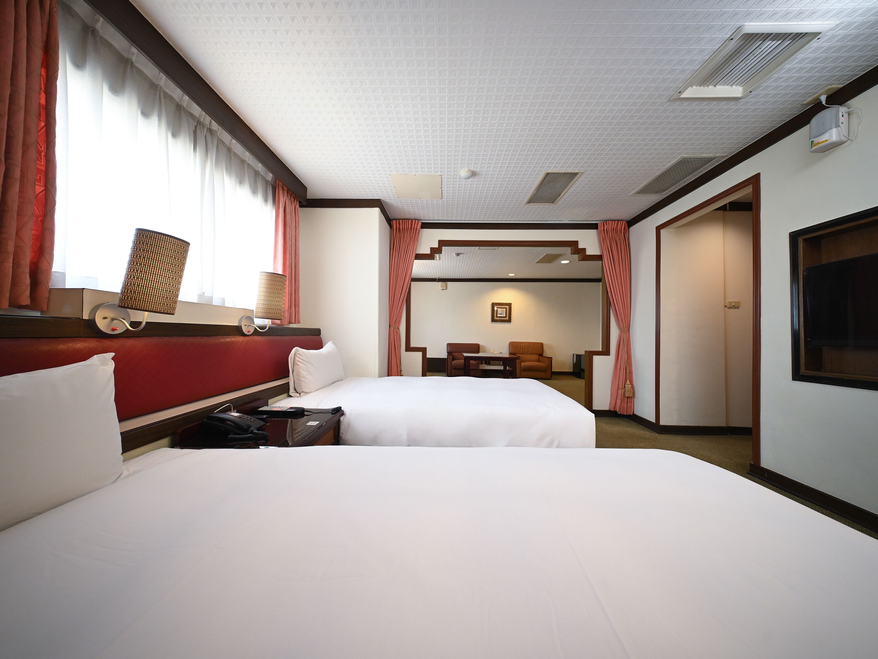 A hotel room with two beds, a desk, a chair, a TV, and a window with curtains.