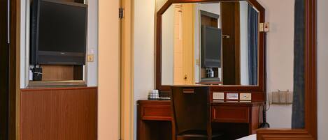 Habitación de hotel con una cama, un escritorio con silla, televisor, espejo y puerta.