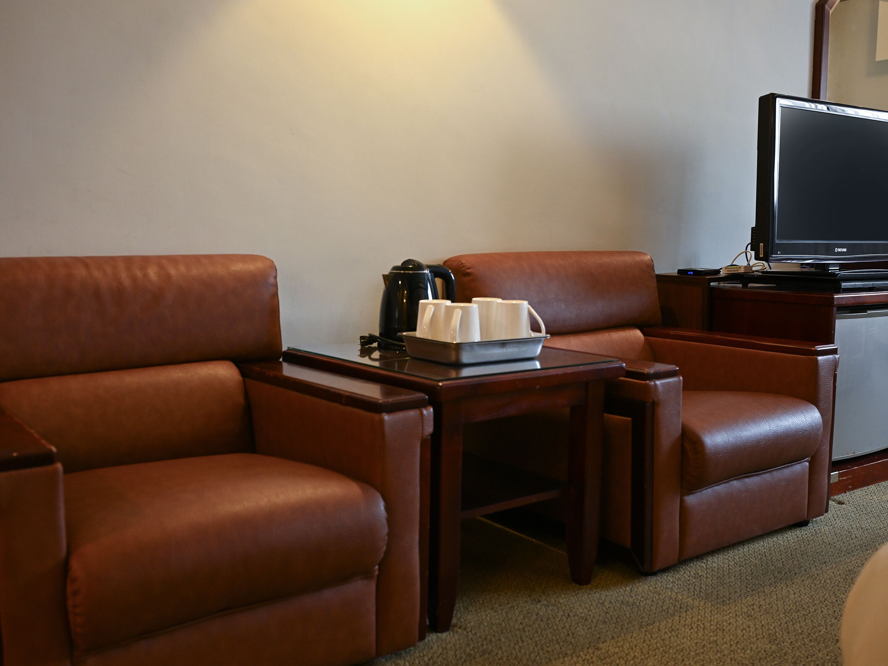 A hotel room with leather armchairs, a small table with a coffee pot and cups, and a television.