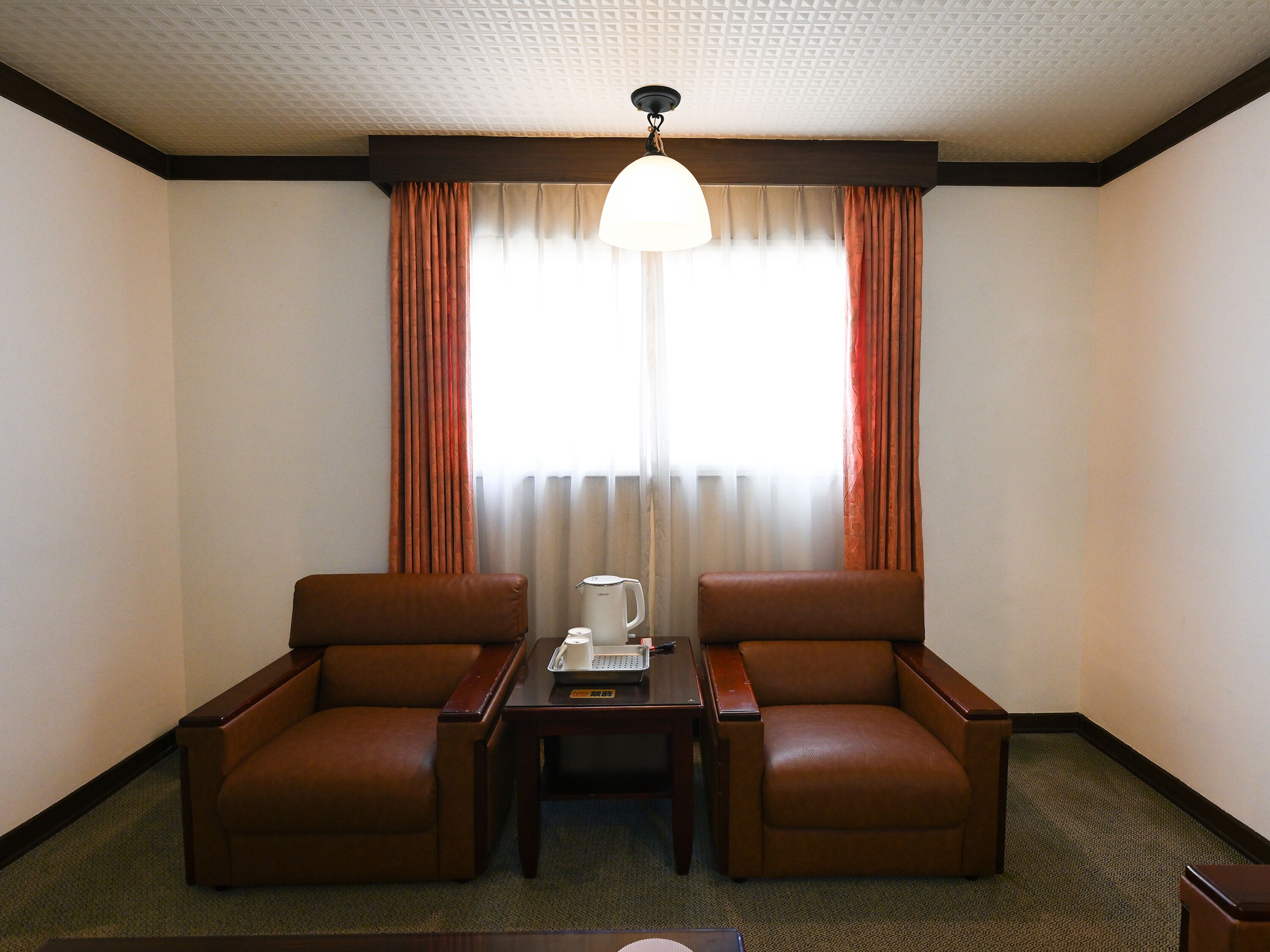 A hotel room with two leather armchairs, a small table with a coffee maker, and a large window with curtains.