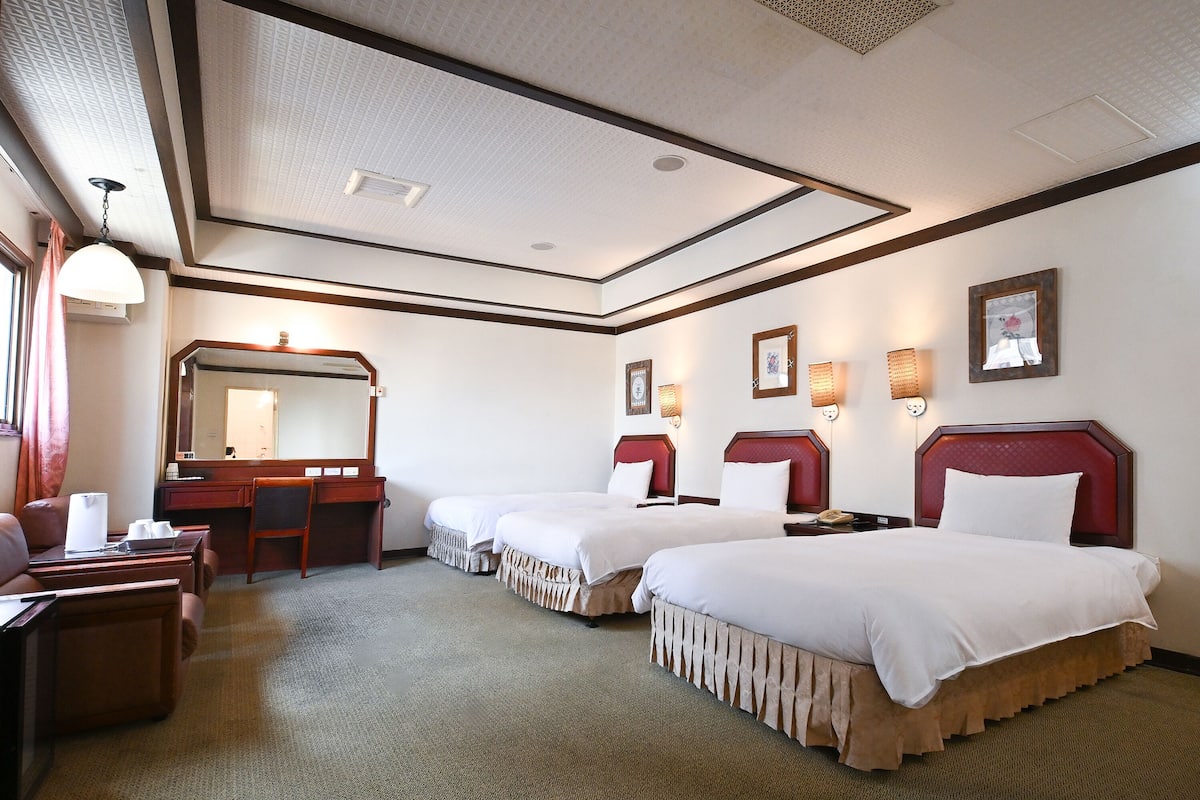 A hotel room with two beds, a desk, a chair, a mirror, and a carpeted floor.