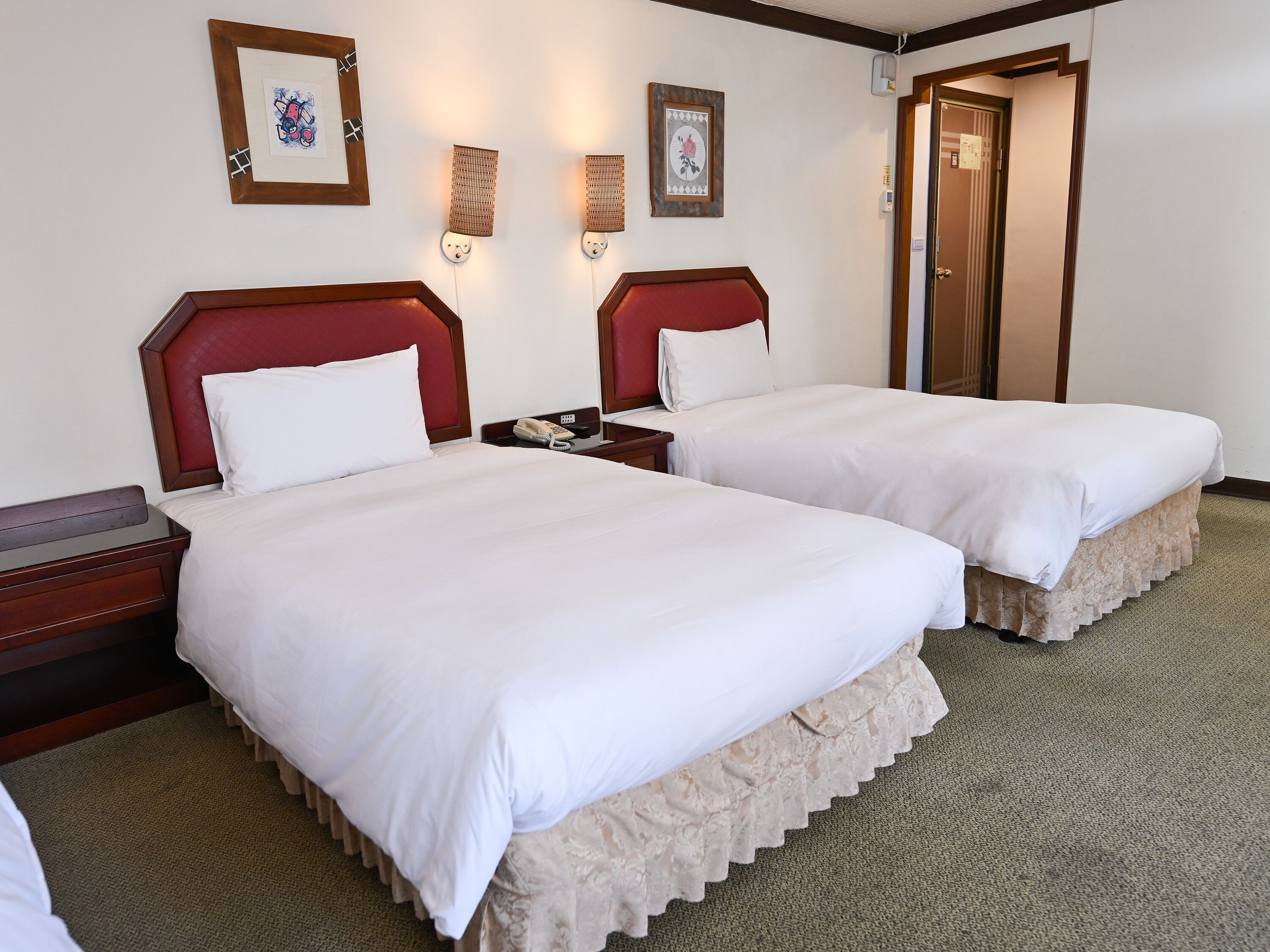 A hotel room with two beds, a telephone, and framed artwork on the wall.