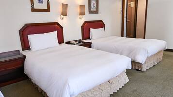 A hotel room with two beds, a telephone, and framed artwork on the wall.