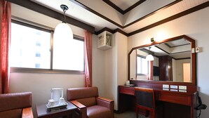 Una habitación de hotel con escritorio, dos sillones de cuero, un espejo grande y una ventana con cortinas.