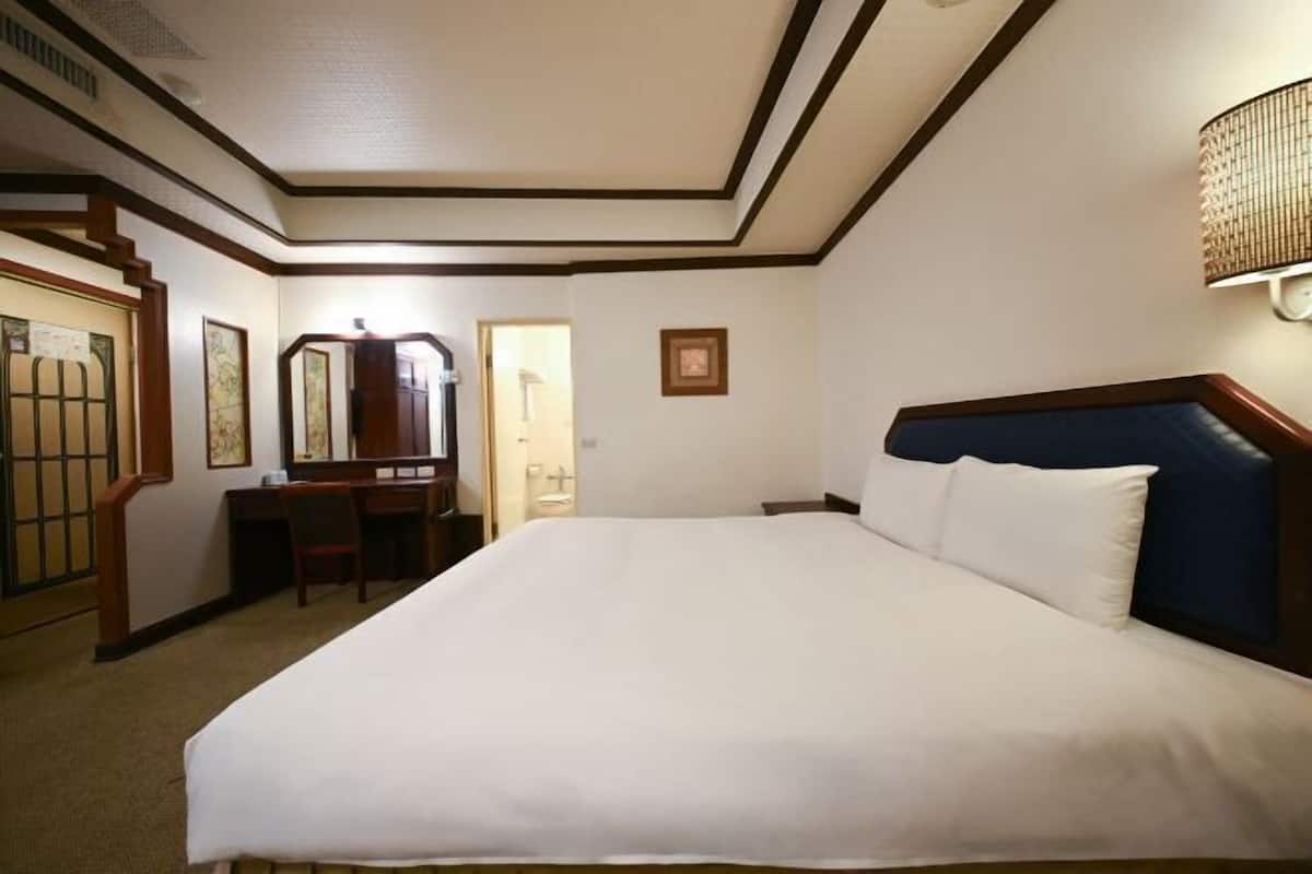 A hotel room with a large bed, a desk, a chair, a mirror, and a door.