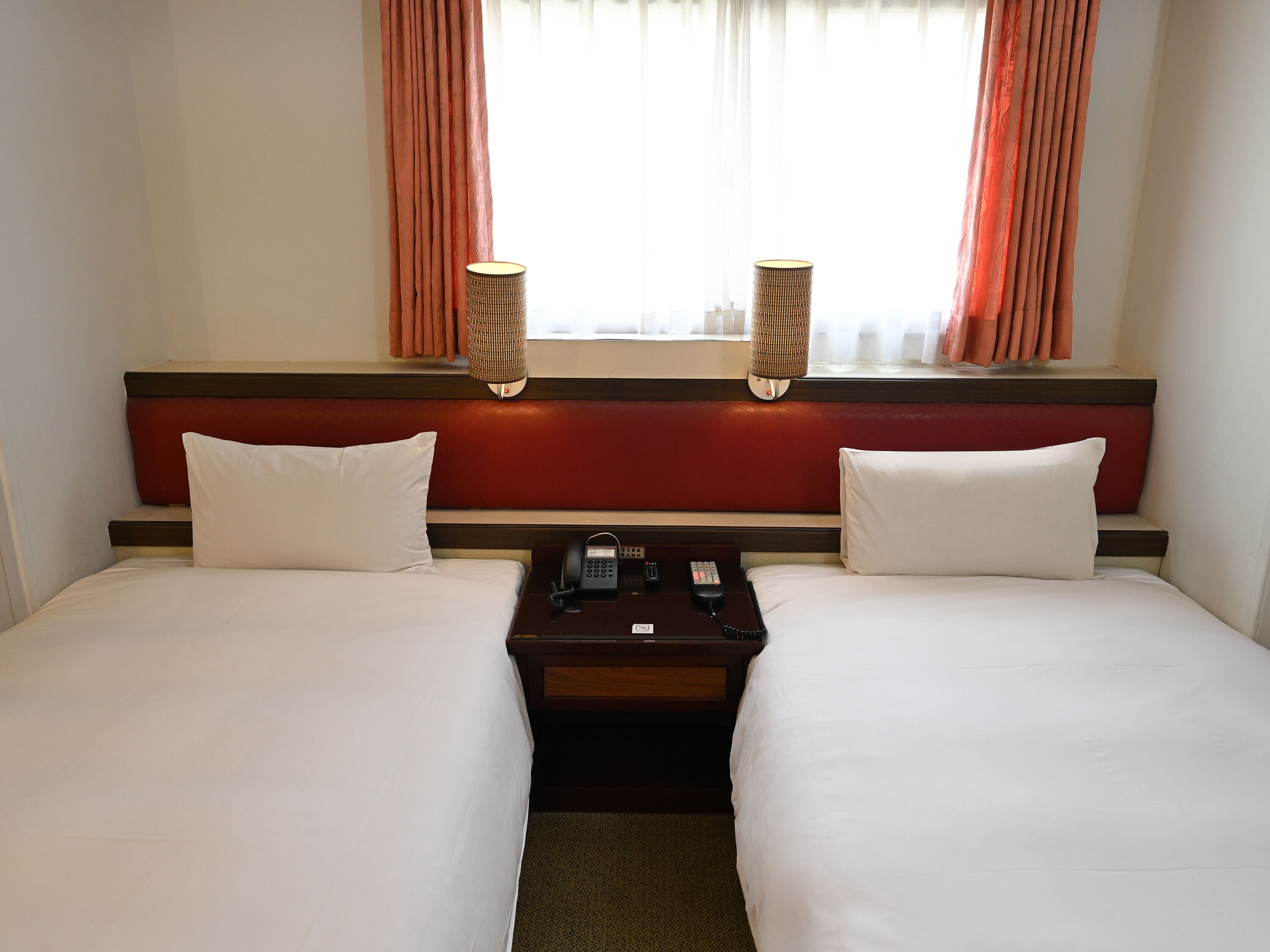 Une chambre d’hôtel avec deux lits, une table de chevet avec un téléphone et une fenêtre avec des rideaux.