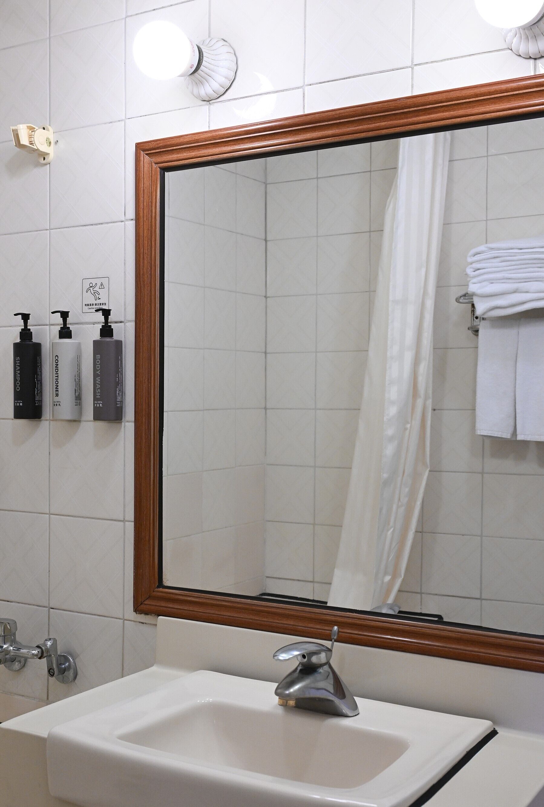 A bathroom with a large mirror, a sink, and three toiletries on the wall.