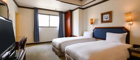 Habitación de hotel con dos camas, un escritorio, televisión y ventana con cortinas.