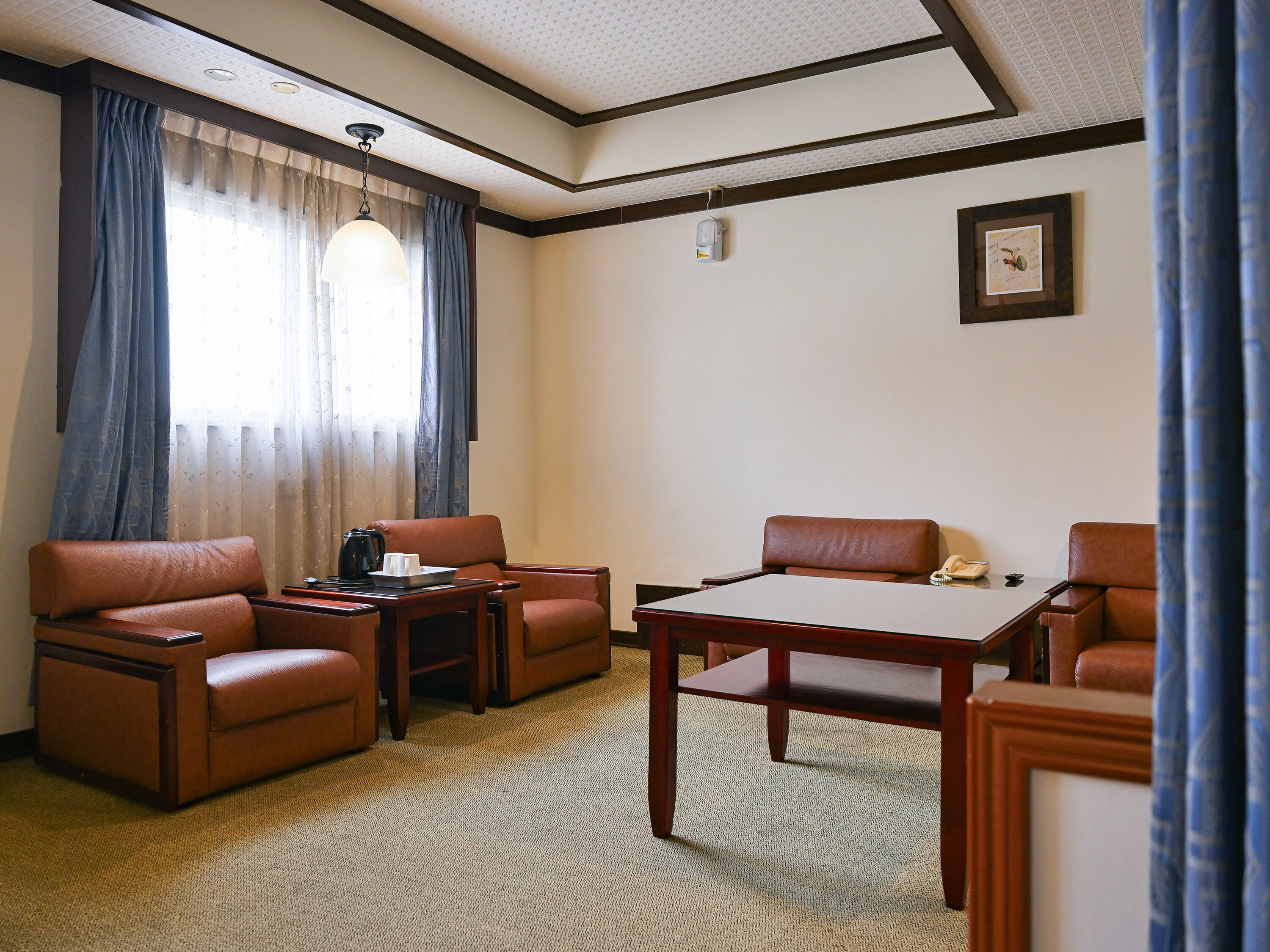 Una habitación de hotel con zona de estar, una mesa y una ventana con cortinas.