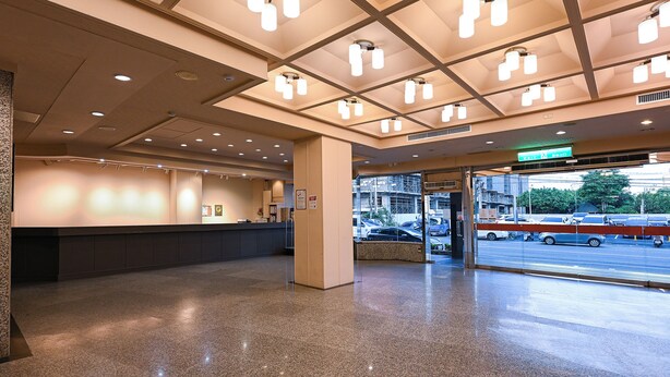 Un vestíbulo de hotel con un mostrador de recepción, una entrada de vidrio al área de estacionamiento e iluminación empotrada en el techo.