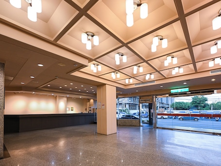 A hotel lobby with a reception desk, a glass entrance to the parking area, and a ceiling with recessed lighting.. Guide Hotel Chunghua Jhongjheng