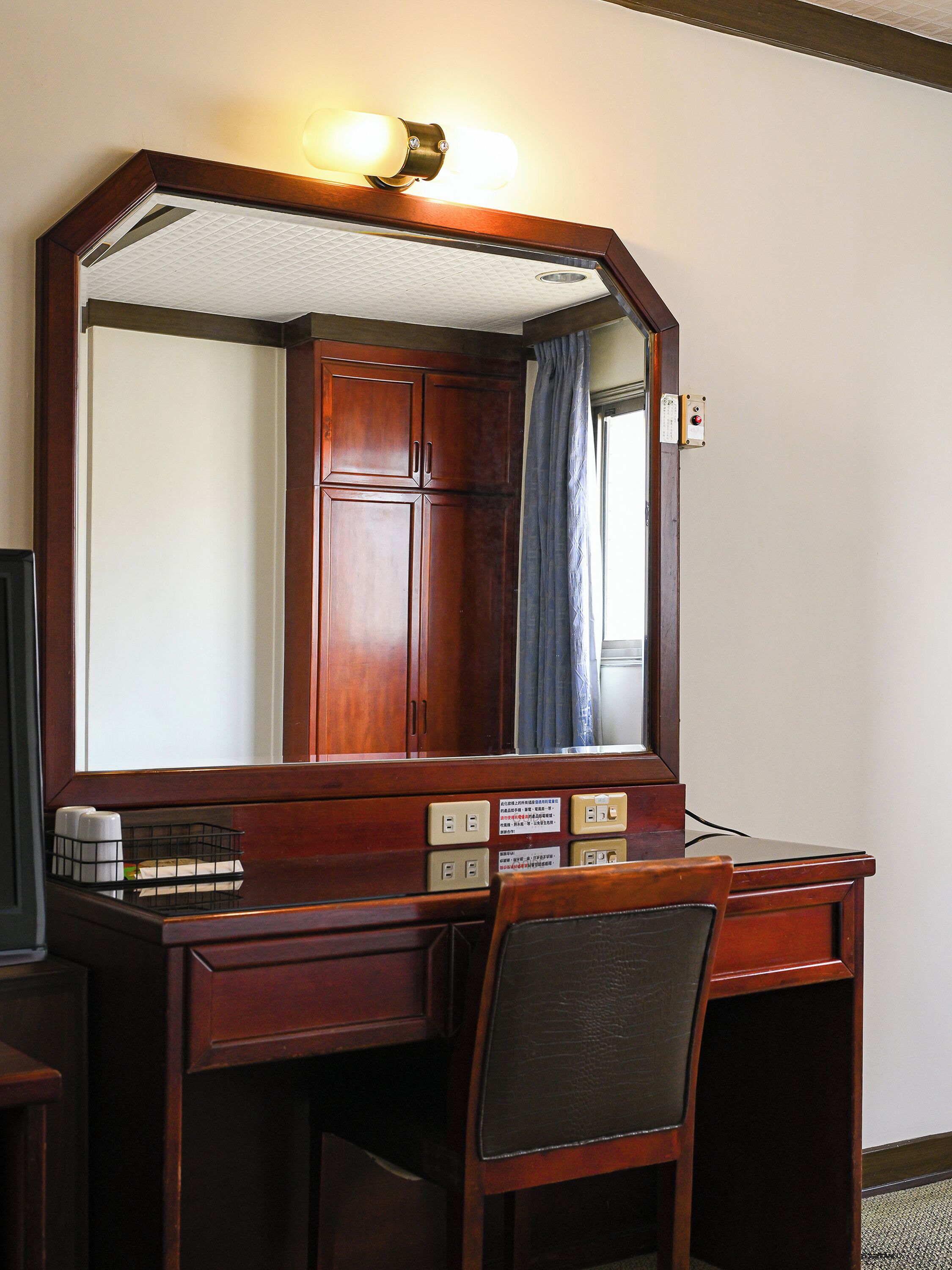 A wooden desk with a mirror, a chair, and a light fixture above the mirror.