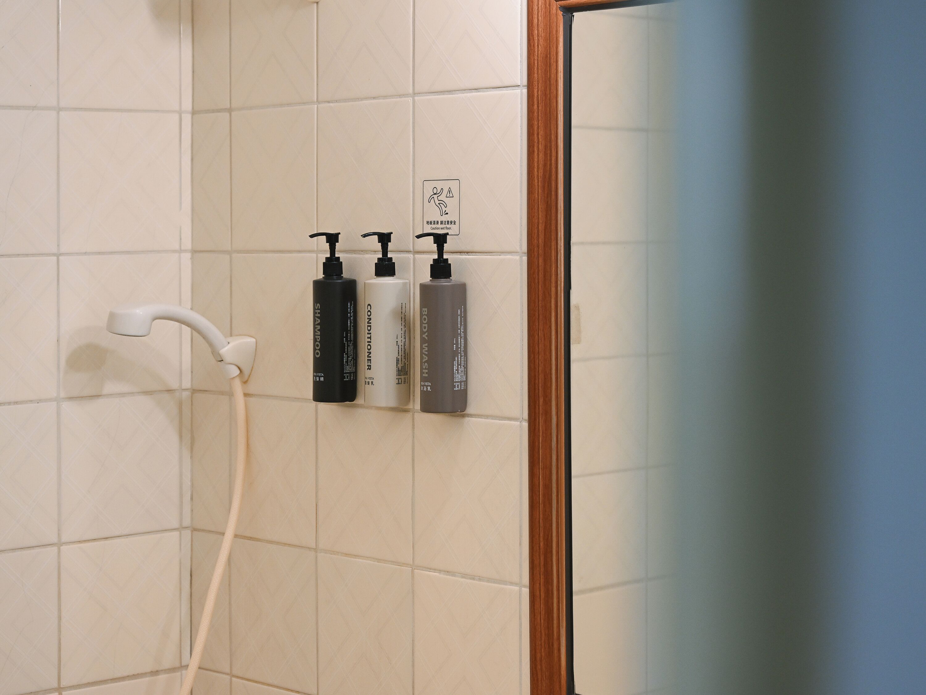 A bathroom with a shower, three toiletry bottles, and a caution sign.