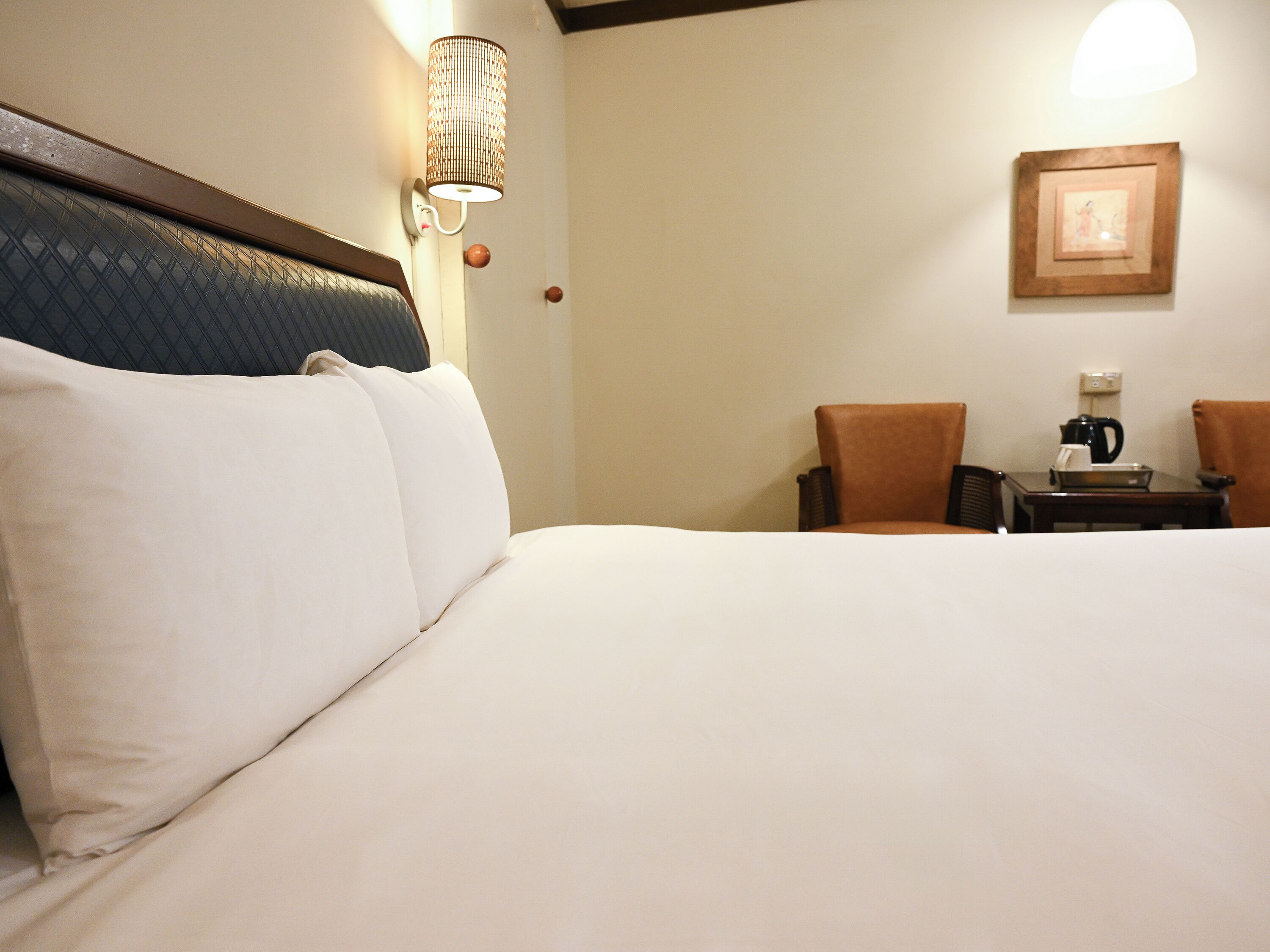 Una habitación de hotel con una cama grande, un escritorio con cafetera y una lámpara de pared.
