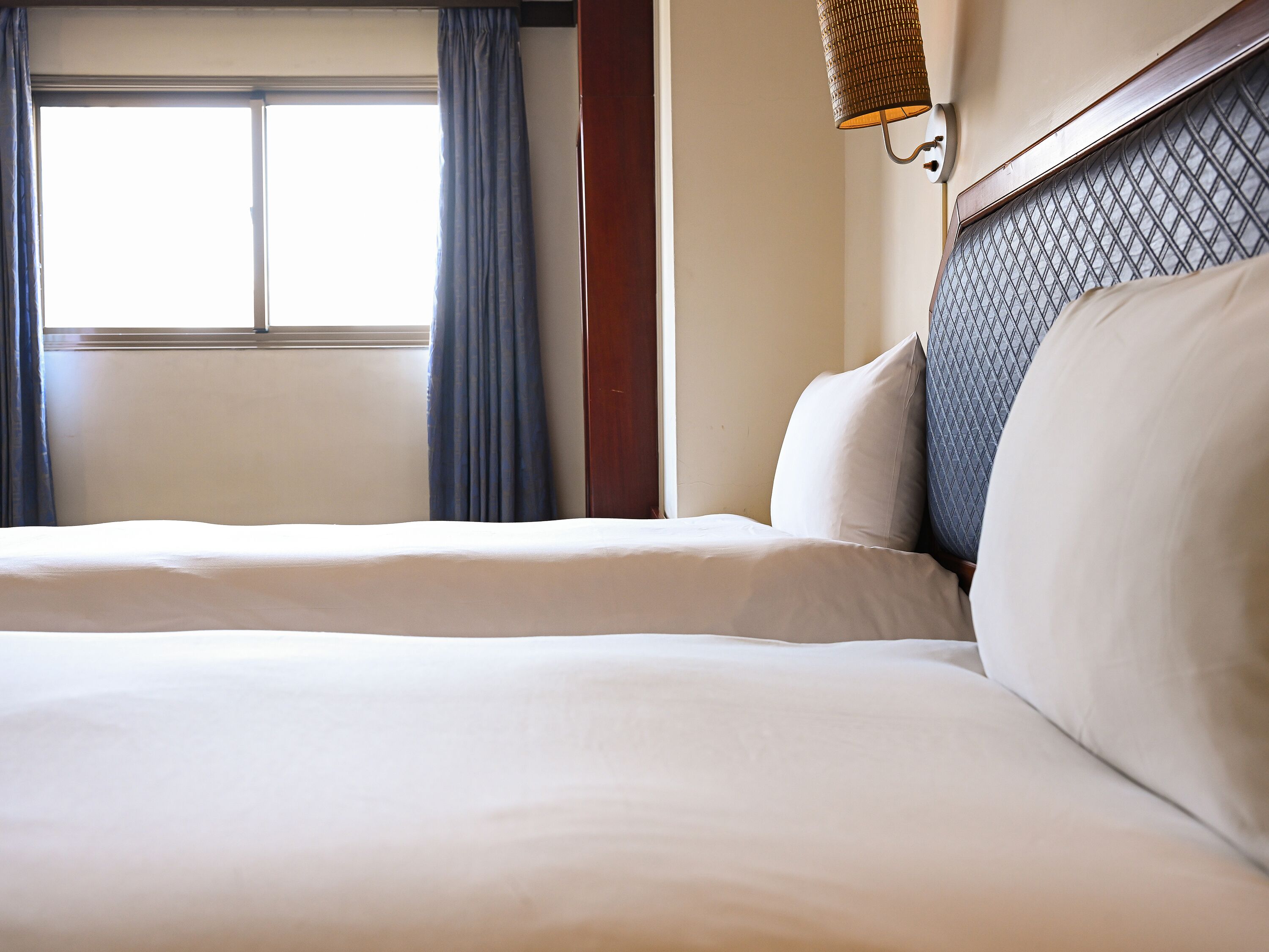 Une chambre d’hôtel avec un grand lit, une fenêtre avec des rideaux et une lampe fixée au mur.
